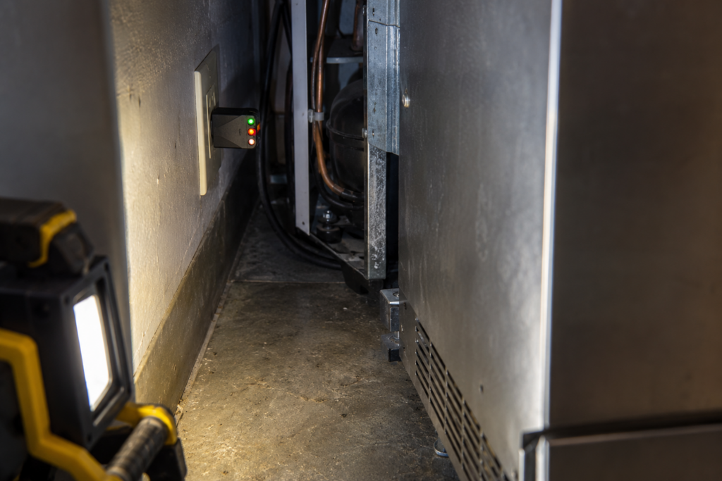 A plug-in receptacle tester with three indicator lights in a wall outlet behind a pulled-forward cabinet.