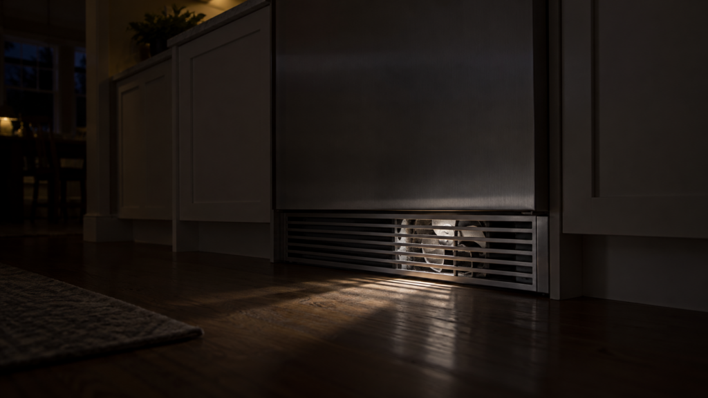 A flashlight beam through the slatted toe grille of a built-in cabinet shows a still fan blade behind it.